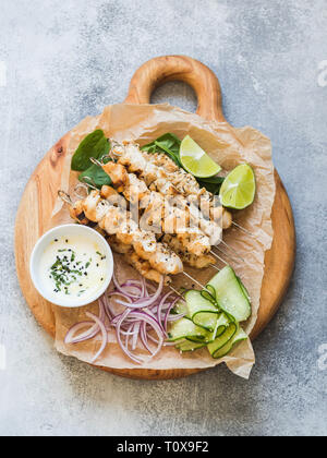 Gegrilltes Hähnchen auf Metall Spieße auf Spinatblättern, Scheiben Gurken, rote Zwiebel und Kalk und Sauce in eine Schüssel geben. Stockfoto