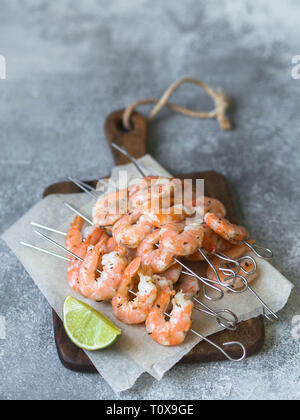 Rote Garnelen auf Metall Spieße mit Limettensaft auf Holz Board auf grauem Hintergrund. Stockfoto