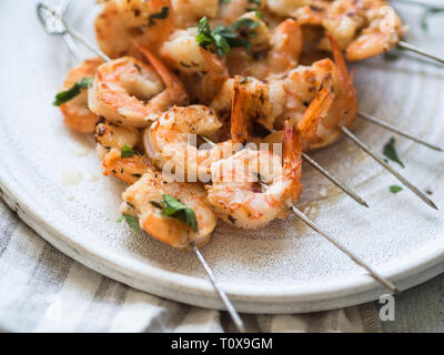 Gegrillte pikante Garnelen auf Metall Spieße mit Petersilie und Limettensaft auf weiße Platte Stockfoto