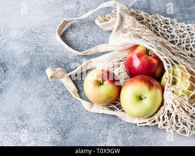Umweltfreundliche beige Einkaufstasche mit roten Äpfeln auf grauem Hintergrund. String Beutel mit Früchten. Null Abfall, kein Plastik Konzept. Stockfoto