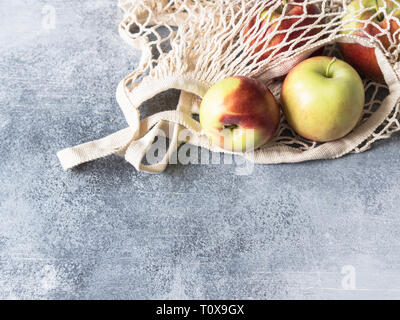 Umweltfreundliche beige Einkaufstasche mit roten Äpfeln auf grauem Hintergrund. String Beutel mit Früchten. Null Abfall, kein Plastik Konzept. Stockfoto