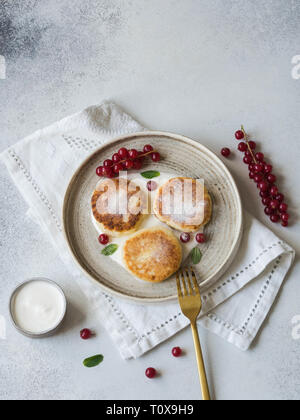 Hausgemachten Käse Kuchen aus Quark serviert auf einem weißen Keramikplatte mit Minze, Sauerrahm und Rote Johannisbeere auf grauem Hintergrund. Stockfoto