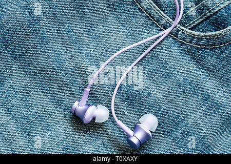 Kopfhörer auf der Oberfläche der blauen Jeans. Das Konzept der Musik, Sport, aktiven Lebensstil Stockfoto