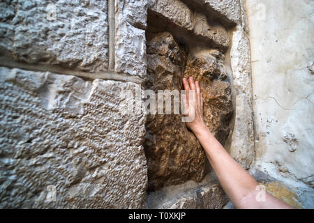 Nahaufnahme der Hand des jungen Mannes Berühren einer alten Platz Stein mit einem Hohlraum, der den Impressum Jesu Hand zu sein. Handprint Jesu am Bahnhof f Stockfoto