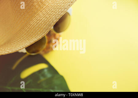 Frische reife Ananas mit Sonnenbrille, Hut und ein Blatt von monstera Baum auf farbigen Hintergrund, Ansicht von oben. Stockfoto