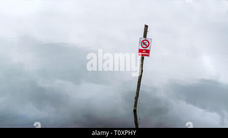 Ein Zeichen der Verbot von Baden auf eine hölzerne Stange in der Stagnierenden blaue Wasser eines Sees mit Nebel und Wolken Stockfoto