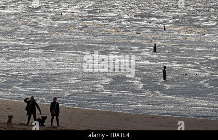 Leute gehen mit ihren Hunden am Crosby Beach in Merseyside neben Anthony's Gormley" an einen anderen Ort "eisernen Männer Skulpturen. Stockfoto