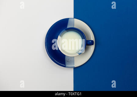 Blau und Weiß Kaffeebecher mit frischer Milch ruht auf einem blauen und weißen Hintergrund gefüllt Stockfoto