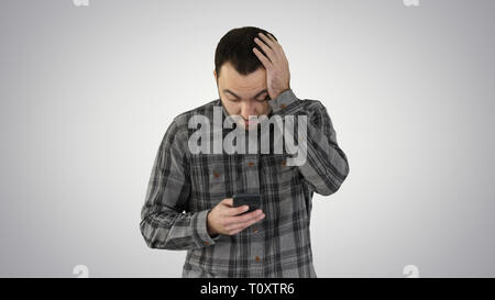 Betont jungen Mann überrascht, schockiert, entsetzt und gestört, durch das, was er sieht auf seinem Handy auf Farbübergang Hintergrund. Stockfoto