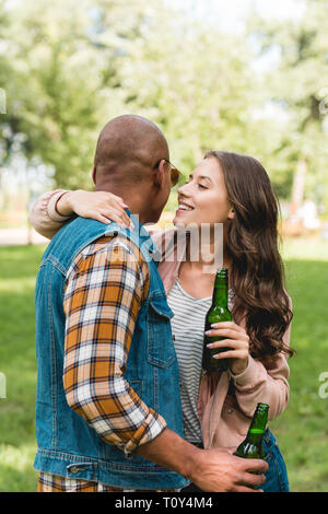 Fröhliches Mädchen das Flüstern im Ohr des afrikanischen amerikanischen Freund Halten Sie Flasche Stockfoto