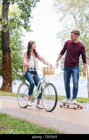 Schöner mann Longboarden und Suchen zu attraktiven Freundin Reiten Fahrrad Stockfoto