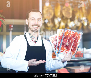 Männliche Verkäufer demonstrieren in Scheiben geschnittenen Speck in Metzgerei Stockfoto