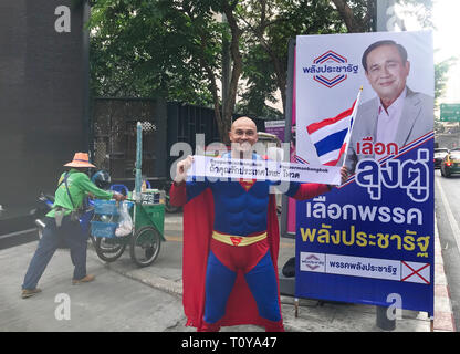 Bangkok, Thailand. 22 Mär, 2019. Die German-Thailander David Pfizenmaier (40) aus Waiblingen ist auf seine Weise als 'Superman' auf den Straßen von Thailands Hauptstadt Bangkok zu den Parlamentswahlen zu verschieben dieser Sonntag. Sein banner sagt: "Wenn sie Thailand Liebe, klicken Sie stimmen." Fünf Jahre nach dem letzten Militärputsch, mehr als 51 Millionen Menschen aufgerufen, zu stimmen. Pfizenmaier steht vor einem Wahlplakat des amtierenden Ministerpräsidenten, allgemeine Prayut Chan-o-cha. (Dpa: 'Thai Schwäbische will, um Menschen wie 'Superman' Credit): Christoph Sator/dpa/Alamy Leben Nachrichten Abstimmung Stockfoto