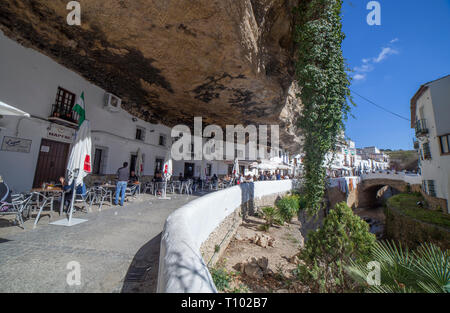 Setenil, Spanien - 4. März, 2019: Straße mit Wohnungen in Felsen Überhänge gebaut. Setenil de las Bodegas, Cadiz, Andalusien, Spanien. Restaurant des sonnigen Höhlen Stockfoto