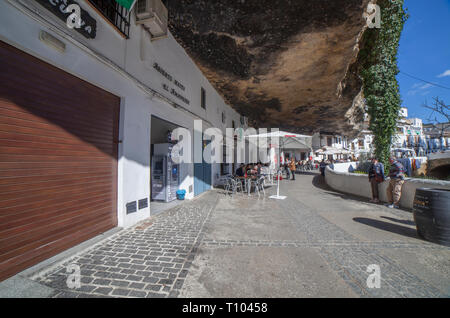 Setenil, Spanien - 4. März, 2019: Straße mit Wohnungen in Felsen Überhänge gebaut. Setenil de las Bodegas, Cadiz, Andalusien, Spanien. Restaurant des sonnigen Höhlen Stockfoto