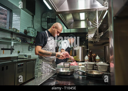 Nur hohe Qualität. Konzentriert Chef mit Tattoos auf seinem Arme frisches dunkles Fleisch ant über zukünftige Gericht denken. Kulinarische Konzept. Stockfoto
