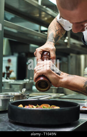 Die letzten Details. Vertikale Foto von jungen männlichen Chef mit mehreren Tattoos auf seinem Arme hinzufügen Pfeffer Pasta Italienisch. Essen Konzept Stockfoto