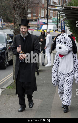 Chassidischer Mann in einem schwarzen Hut mit einer Flasche Wein begleitet eine Jugend als Dalmatiner für das Jüdische Purimfest Fancy Dress feiern gekleidet Stockfoto