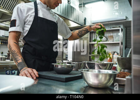 Vegetarisches Essen. Nahaufnahme der Koch die Hände mit schönen Tattoos Vorbereitung Salat in einem Restaurant Küche. Kochen Stockfoto