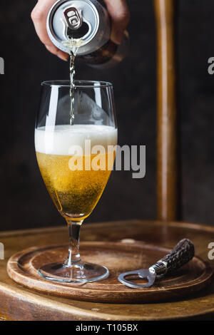 Bier ins Glas gießt aus einer Blechdose auf dunklem Hintergrund Stockfoto