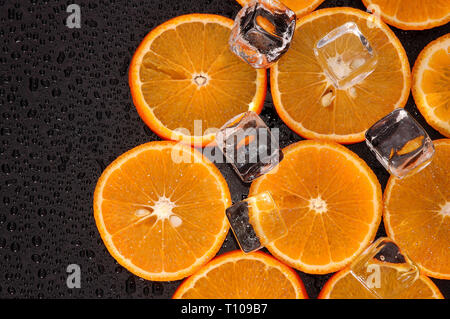 Orange Scheiben mit Eiswürfeln auf nassen Schwarzen Tisch Stockfoto