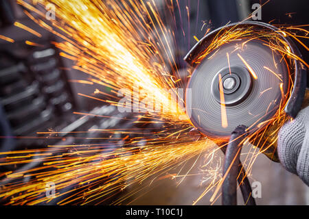 Eine Nahaufnahme von einem Automechaniker mit einem Metall Grinder ein Auto in eine Werkstatt zu schneiden, helle Blitze fliegen in verschiedene Richtungen, in die Stockfoto