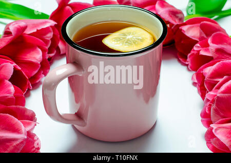 Rosa Tasse Tee mit Zitrone steht auf einem weißen Hintergrund Neben rosa Tulpen. closeup Stockfoto