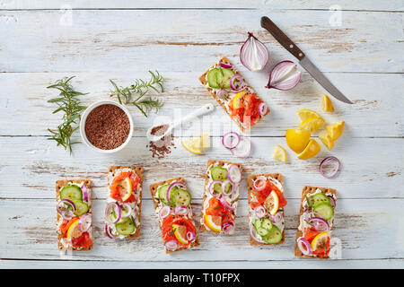 Dünne Sauerteig Roggen Knäckebrot lachs Sandwiches mit Gurke, Frischkäse und roten Zwiebeln, bestreut mit Leinsamen auf einem weißen alten Holztisch Stockfoto