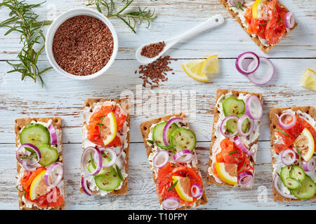 Ansicht von oben von dünnen Sauerteig Roggen Knäckebrot lachs Sandwiches mit Gurke, Frischkäse und roten Zwiebeln, bestreut mit Leinsamen auf einem weißen Stockfoto