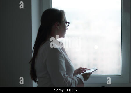 Geschäftsfrau mit einem Smartphone beim Stehen in der Nähe ein Büro Fenster. Stockfoto