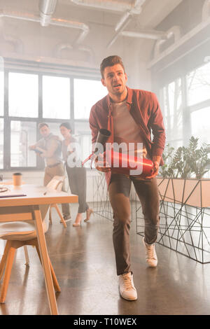 Erschrocken Geschäftsmann holding Feuerlöscher in Office mit Rauch in der Nähe von Kollegen Stockfoto