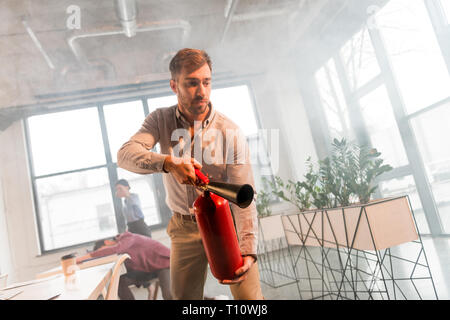 Gut aussehender Geschäftsmann holding Feuerlöscher in Office mit Rauch in der Nähe von Kollegen Stockfoto