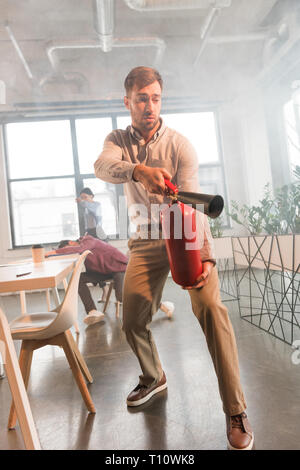 Erschrocken Geschäftsmann holding Feuerlöscher in Office mit Rauch in der Nähe von Kollegen Stockfoto