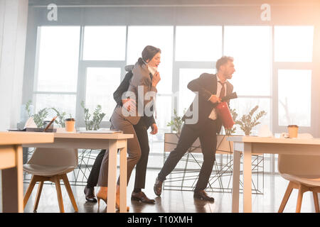 Geschäftsmann holding Feuerlöscher in der Nähe von Kollegen während schreiend in Office mit Rauch Stockfoto