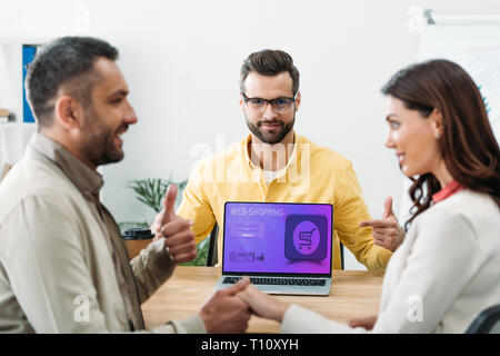 Selektiver Fokus der Advisor zeigt mit dem Finger auf Laptop mit Web shopping Webseite auf dem Bildschirm während Investor holding Frau Hand und blättere in aus Stockfoto