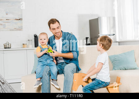 Preschooler junge Reiter aus Holz Schaukelpferd während Vater sitzen und spielen mit Kleinkind Sohn auf der Couch zu Hause Stockfoto