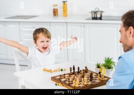 Preschooler Sohn jubelnd die Hände in die Luft, während das Schachspiel mit Vater zu Hause Stockfoto