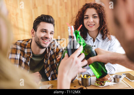 Selektiver Fokus der lächelnden und schöne Freunde jubeln mit Glasflaschen im Cafe Stockfoto