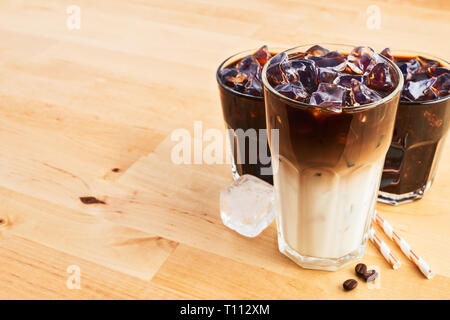 Eiskaffee und Latte macchiato im hohen Glas mit Strohhalm auf hölzernen Tisch. Verschiedene Arten von Kaffee. Kopieren Sie Platz für Text. Stockfoto