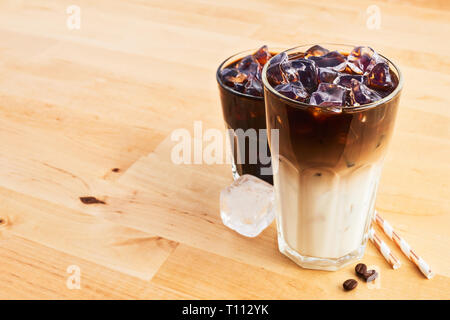 Eiskaffee und Latte macchiato im hohen Glas mit Strohhalm auf hölzernen Tisch. Verschiedene Arten von Kaffee. Kopieren Sie Platz für Text. Stockfoto