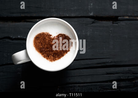 Hohe Betrachtungswinkel und einer Tasse Cappuccino, mit einem Herzen mit Kakaopulver auf dem Milchschaum gezeichnet, auf einem grauen rustikalen Holztisch mit einigen Leerstelle auf Stockfoto