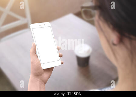 Frau, die weißen smart phone mit isolierten Bildschirm für mockup. Coffee shop Tisch im Hintergrund. Stockfoto