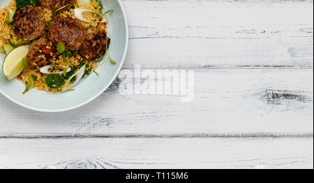 Eine Schüssel mit saftigen Harissa Fleisch Kugeln auf einem Bett von kuskus schoß ein weißes Holz- Hintergrund in ein Banner Format mit Platz für Kopie Stockfoto