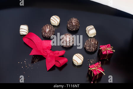 Schokolade und roten gebunden Bogen auf Tisch mit zwei kleinen Requisiten weihnachten Quadrat Geschenk. Weihnachten festliche Dekoration. Stockfoto