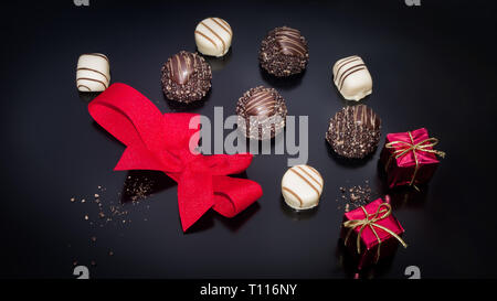 Schokolade und roten gebunden Bogen mit zwei kleinen Requisiten weihnachten Quadrat Geschenk. Trüffel behandelt mit Weihnachten Neujahr Thema Ornamente Hintergrund Stockfoto