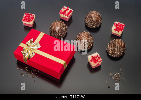 Red velvet Geschenkkarton mit Gold Ribbon auf dunklem Hintergrund, mit luxuriösen Schokoladen. Weihnachten Neujahr gourmet Urlaub Dekoration. Stockfoto