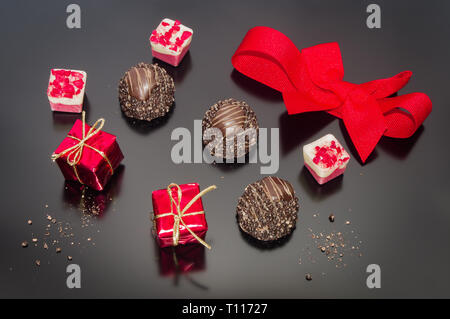 Pralinen Trüffel und roten gebunden Bogen mit zwei kleinen Requisiten weihnachten Quadrat Geschenk. Süße Weihnachten festliche Dekoration. Stockfoto