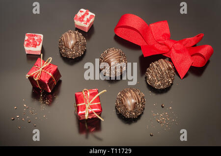 Schokolade Pralinen Trüffel für Weihnachten in Rosa und Rot mit roter Schleife gebunden. Zwei kleine Requisiten weihnachten Quadrat Geschenk. Festliche Dekoration. Stockfoto