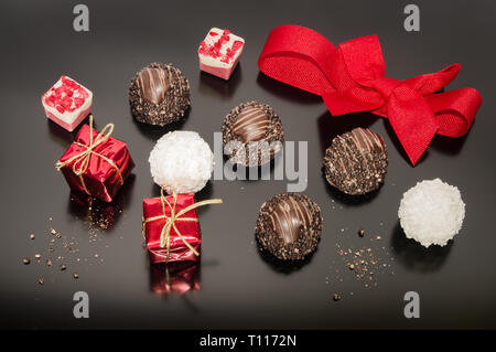 Schokolade Pralinen Trüffel und rote Schleife gebunden in Bogen und zwei kleine Requisiten Weihnachten Quadrat Geschenk. Dekoration für Weihnachten. Festliche Dekoration Stockfoto