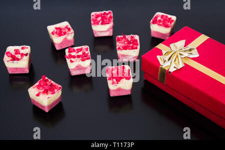 Geschenk verpackt in Red Box mit Gold Ribbon in Bogen mit milchig Schokolade Hintergrund gebunden. Stockfoto